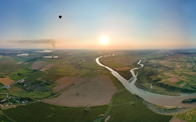 Vista aérea de un pequeño globo aerostático volando sobre el campo rural al atardecer