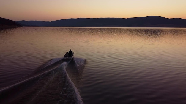 Vista aérea de un pescador en un bote de motor de velocidad pescando en un lago con un hermoso amanecer