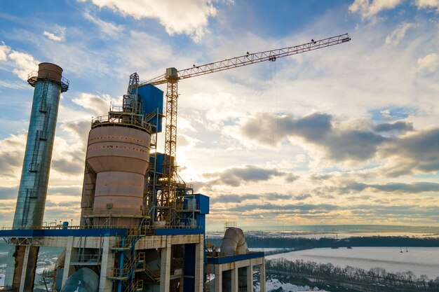 Vista aérea de la planta de cemento con alta estructura de fábrica y grúa torre en el área de producción industrial.