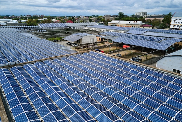 Vista aérea de la planta de energía solar con paneles fotovoltaicos azules montados en el techo de un edificio industrial para producir electricidad ecológica verde. Producción de concepto de energía sostenible.