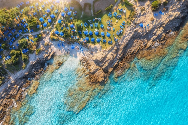 Vista aérea de la playa de arena de la bahía del mar con sombrillas, piedras y rocas en el agua al atardecer en verano Cerdeña Italia Paisaje tropical con laguna marina nadando gente agua azul Drone vista desde arriba