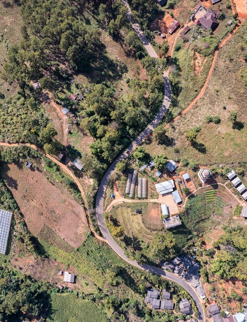 Vista aérea del pueblo rural local con camino de ripio a través del valle en el campo lejano entre la selva tropical en el sudeste asiático