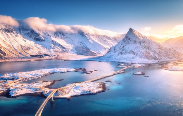 Foto vista aérea del puente sobre el mar y las montañas nevadas en las islas lofoten noruega puentes de fredvang al atardecer en invierno paisaje con rocas de agua azul en la carretera de nieve y el cielo con clloads vista superior