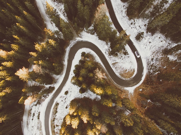 Vista aérea de la sinuosa carretera curva con coche y bosque de otoño con árboles de color otoñal en Italia