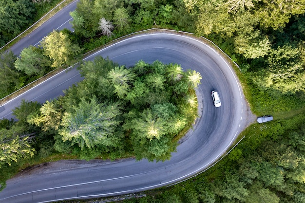 Vista aérea de la sinuosa carretera en el paso de alta montaña a través de densos bosques de pinos verdes.