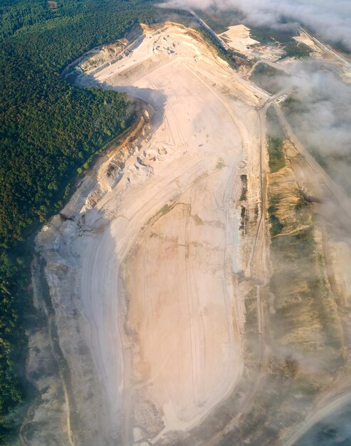 Vista aérea del sitio de minería a cielo abierto de extracción de materiales de piedra caliza para la industria de la construcción con excavadoras y volquetes.