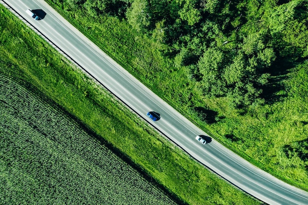Vista aérea superior de una carretera asfaltada con un coche a través del bosque xAgreen y el campo de maíz en verano
