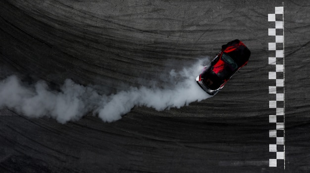 Vista aérea superior del coche a la deriva en la pista de carreras con línea de meta y mucho humo de neumáticos en llamas.