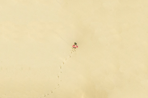 Vista aérea superior do jovem solitário andar no deserto sobre a textura da areia. conceito perdido