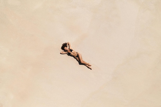Vista aérea superior de drones de mujer en bikini de traje de baño relajándose y tomando el sol en la playa de arena blanca