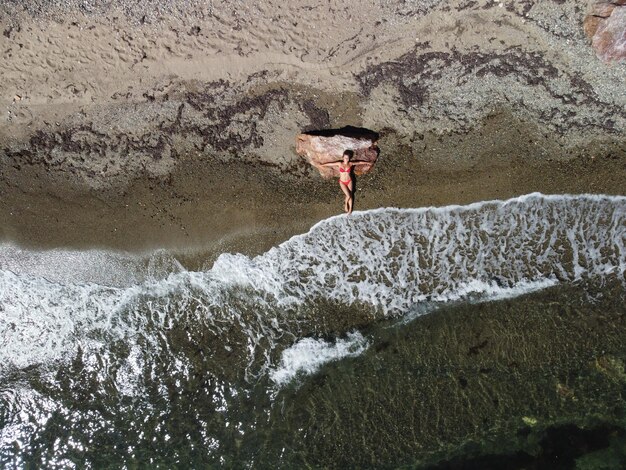 Vista aérea superior em uma jovem loira sensual de biquíni vermelho deitada na rocha perto da água no mar