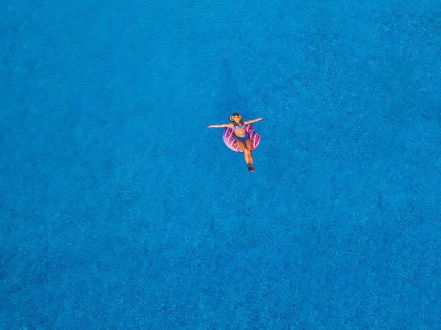 Vista aérea superior de la hermosa niña en la piscina desde arriba, relajarse, nadar en un anillo inflable y divertirse en el agua en vacaciones familiares