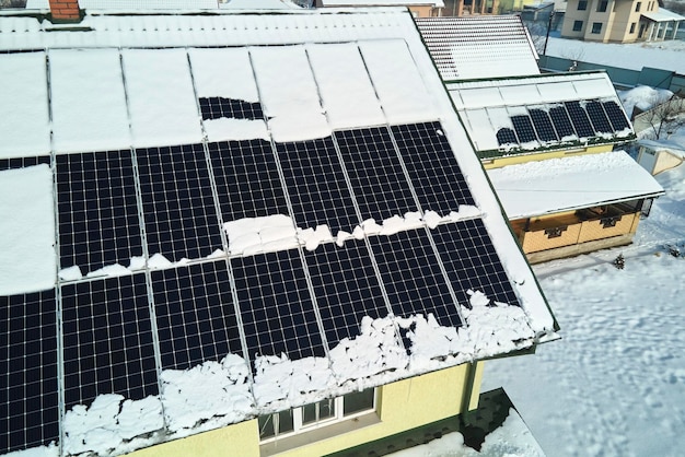 Vista aérea del techo de una casa con paneles solares cubiertos de nieve que se derrite al final del invierno para producir energía limpia Concepto de baja eficacia de la electricidad renovable en la región norte