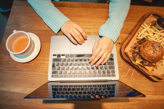 Vista aérea tipo de manos en el teclado hamburguesa de mesa de madera con taza de té