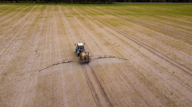 Vista aérea del tractor agrícola arando y rociando en el campo