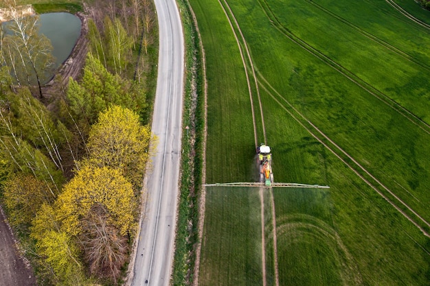 Vista aérea del tractor rociando los productos químicos en el gran campo verde