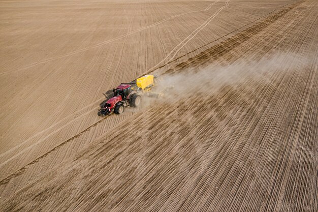 Vista aérea del tractor con sembradora montada realizando siembra directa de cultivos en campo agrícola arado. El agricultor está utilizando maquinaria agrícola para el proceso de plantación, vista superior