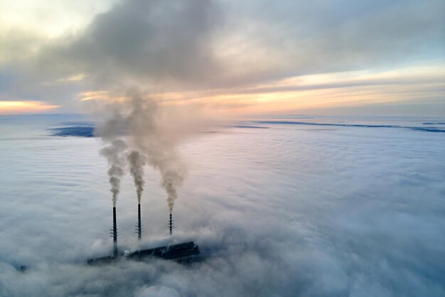 Vista aérea de las tuberías altas de la central eléctrica de carbón con humo negro que sube por la atmósfera contaminante al atardecer.