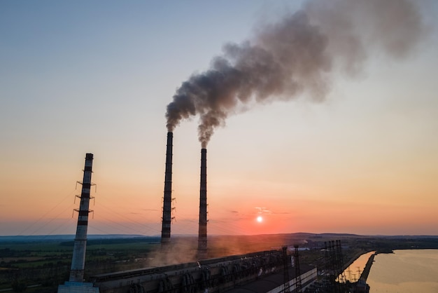 Vista aérea de las tuberías altas de la planta de energía de carbón con humo negro que se mueve hacia arriba contaminando la atmósfera al atardecer. Producción de energía eléctrica con concepto de combustible fósil.