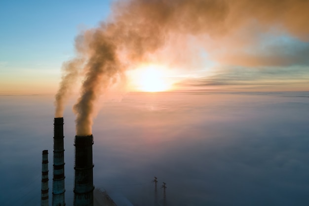 Vista aérea de los tubos altos de la planta de energía de carbón con humo negro subiendo la atmósfera contaminante al atardecer.