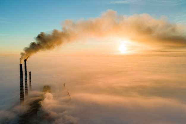 Vista aérea de los tubos altos de la planta de energía de carbón con humo negro subiendo la atmósfera contaminante al atardecer.