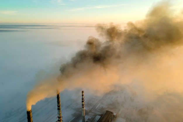 Vista aérea de los tubos altos de la planta de energía de carbón con humo negro subiendo la atmósfera contaminante al atardecer.