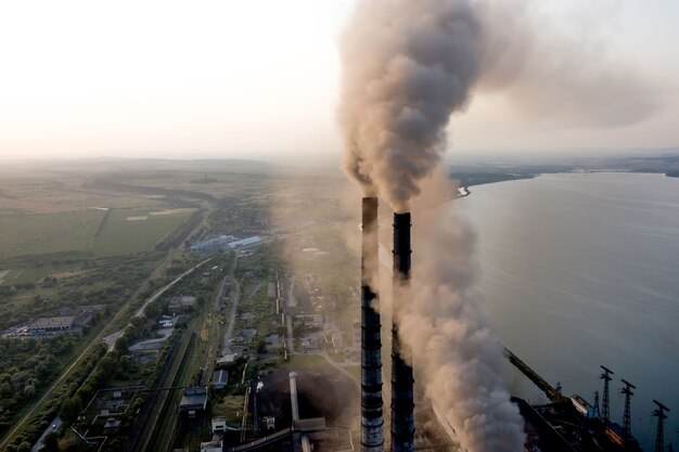 Vista aérea de los tubos altos de la planta de energía de carbón con humo negro subiendo la atmósfera contaminante al atardecer.