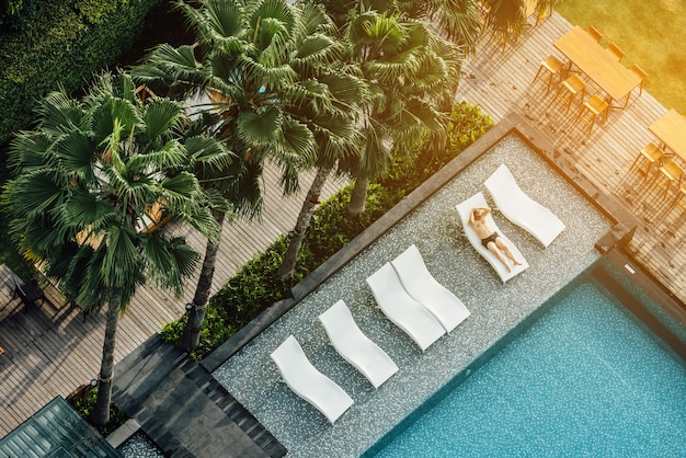 Vista aérea del turista se tumbó en sillas al aire libre cerca de la piscina con palmeras en la zona del hotel.