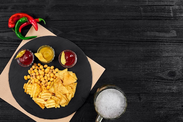 Vista aérea del vaso de cerveza y bocadillos con salsa en la mesa de madera negra