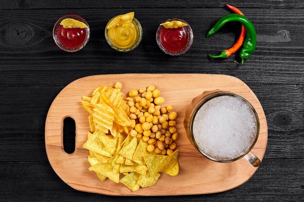 Vista aérea del vaso de cerveza y bocadillos con salsa en la mesa de madera negra