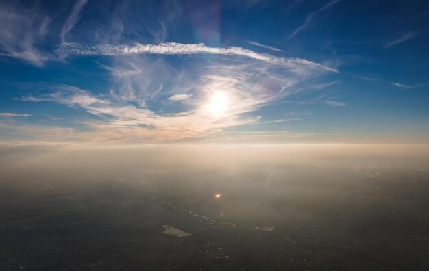 Vista aérea desde la ventana del avión a gran altitud de una ciudad distante cubierta con una capa de niebla fina y niebla y nubes distantes en la noche