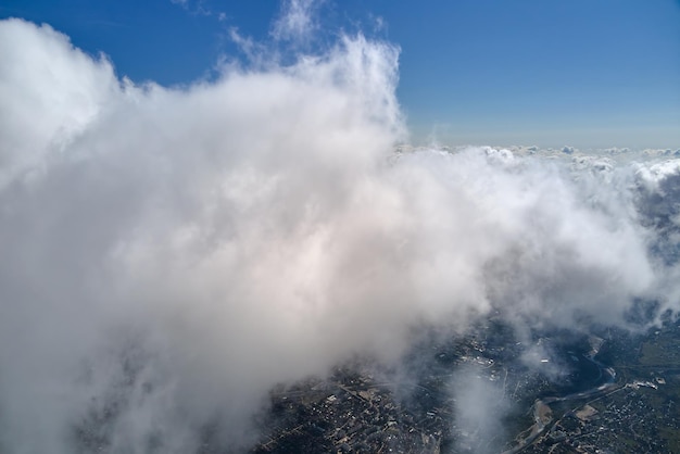 Vista aérea desde la ventana del avión a gran altitud de una ciudad distante cubierta de cúmulos hinchados que se forman antes de la tormenta.
