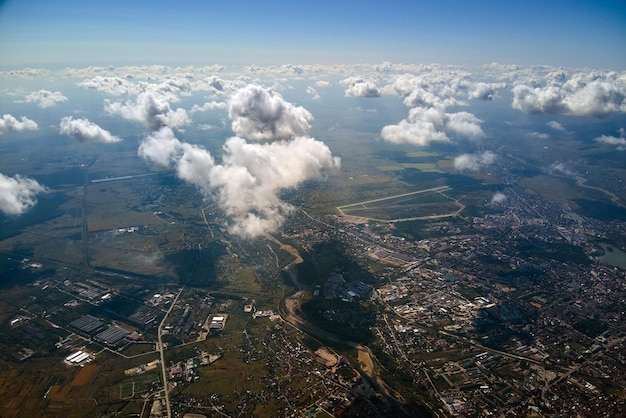 Vista aérea desde la ventana del avión a gran altura de la ciudad distante cubierta con nubes cúmulos hinchadas blancas.