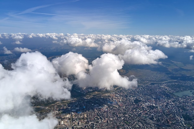 Vista aérea desde la ventana del avión a gran altura de una ciudad distante cubierta de nubes de cúmulos hinchadas blancas