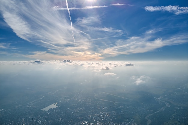 Vista aérea desde la ventana del avión a gran altura de la tierra cubierta con una fina capa blanca de neblina brumosa y nubes distantes.