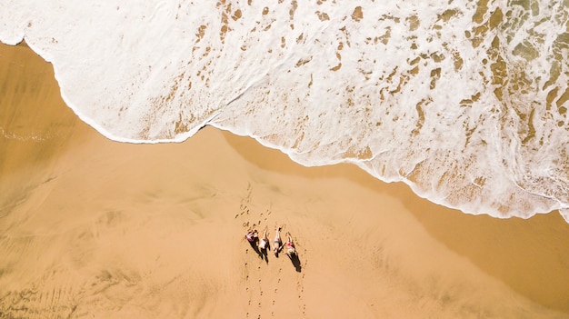 Vista aérea vertical del grupo de jóvenes amigos disfrutando de las vacaciones de verano en la playa con la gran ola que viene