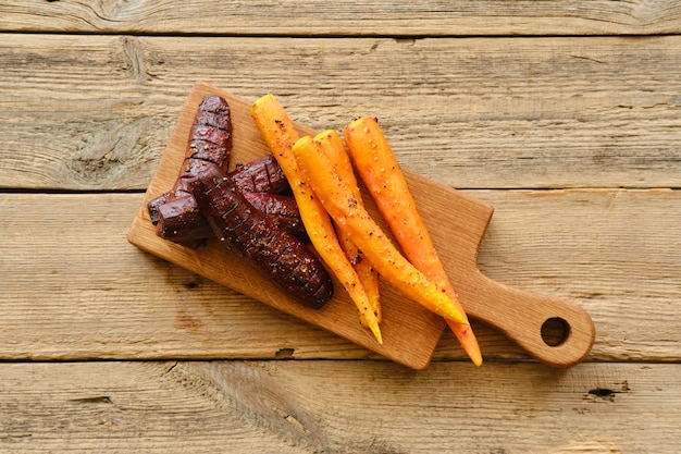 Vista aérea de zanahoria al horno y remolacha con sal y pimienta sobre tabla de madera