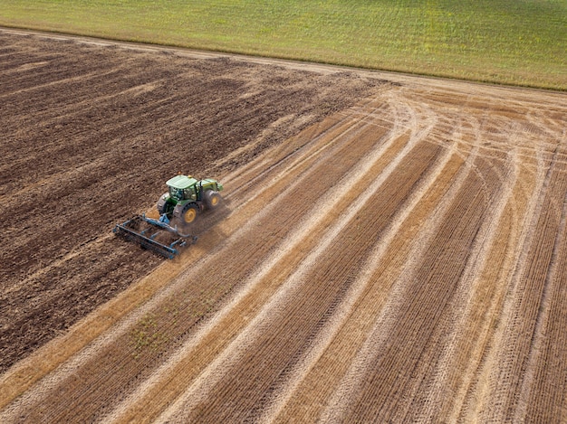 Vista aérea desde el zumbido del campo después de la cosecha. El tractor arando el suelo después de la cosecha en el campo: preparación del suelo para el trabajo de siembra.