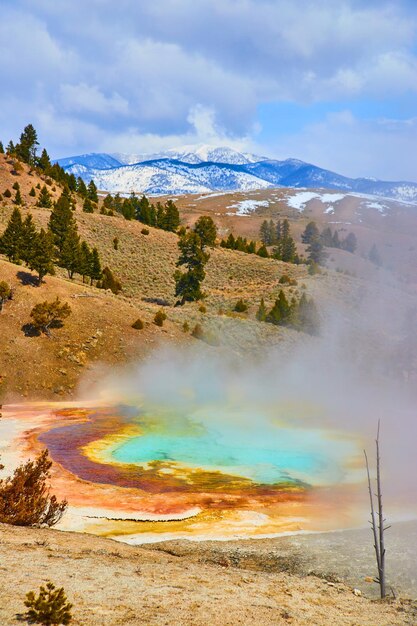 Vista de aguas termales vaporosas desde arriba con vistas a las montañas nevadas por Yellowstone