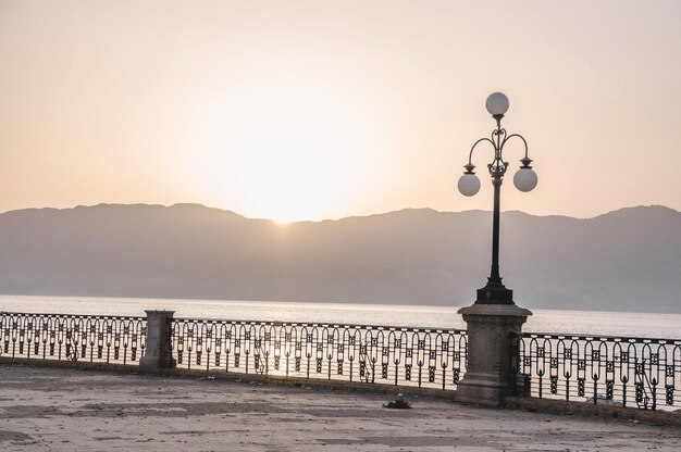 Foto una vista al atardecer de un lago con una valla y un poste de luz