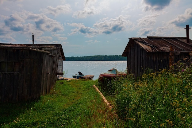 Vista al lago con viejos graneros de madera, pequeño muelle y botes en verano