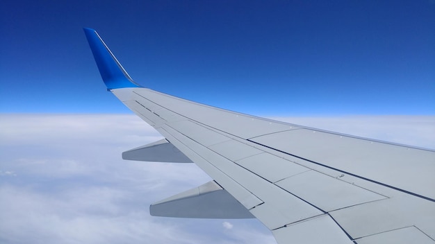 Vista de un ala de avión gris a través de la ventana del avión sobre las nubes