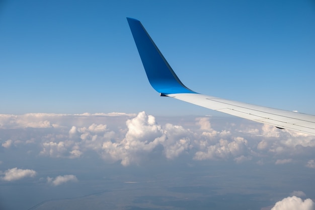 Vista del ala del avión a reacción desde el interior volando sobre nubes blancas en el cielo azul