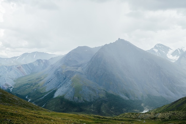 Vista alpina atmosférica da passagem para a grande montanha com o pináculo afiado sob um céu nublado sombrio.