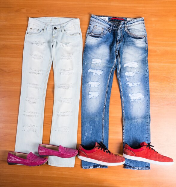 Vista de alto ángulo de él y de ella, jeans azules desgastados y rotos dispuestos sobre una superficie de madera con zapatos a juego: elegantes mocasines rosados y zapatillas rojas