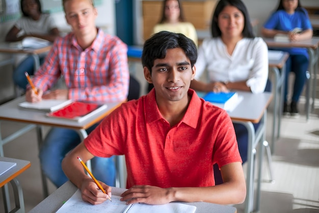 Vista de alto ángulo de un estudiante asiático sonriente escribiendo en el aula.
