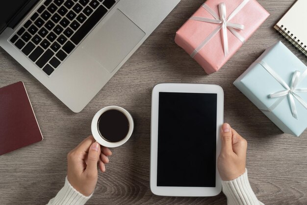 Vista de alto ángulo de una mujer sosteniendo una taza de café con una tableta digital en la mesa