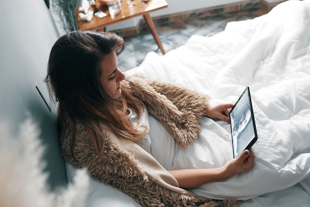 Vista de alto ángulo de una mujer usando una tableta digital mientras está sentada en la cama