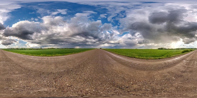 Vista de ángulo de 360 grados de panorama hdri esférico completo en camino de grava húmeda entre campos en el día de primavera con nubes de tormenta después de la lluvia en proyección equirectangular lista para contenido VR AR