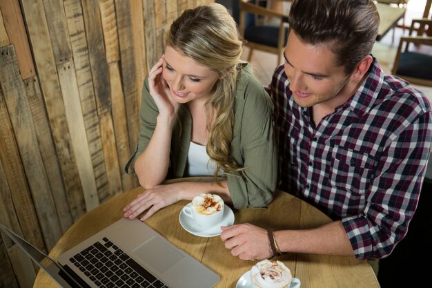 Vista de ángulo alta, de, pareja joven, usar la computadora portátil, en la mesa, en, cafetería